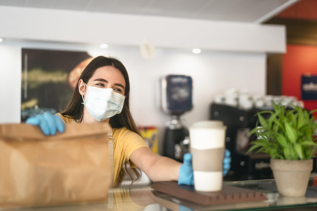 Bar owner working only with take away orders during corona virus outbreak – Young woman worker wearing face surgical mask giving meal to customers – Healthcare and Food drink concept