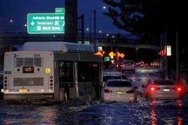 A bus navigates past abandoned cars on a flooded highway in Queens, New York