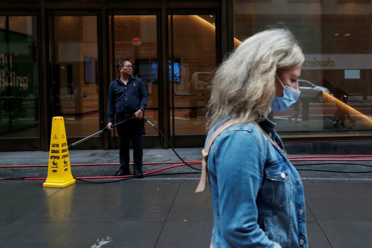 A man pauses while pressure washing a sidewalk, amid the coronavirus disease (COVID-19) pandemic, as a woman walks by with a protective face mask in New York City