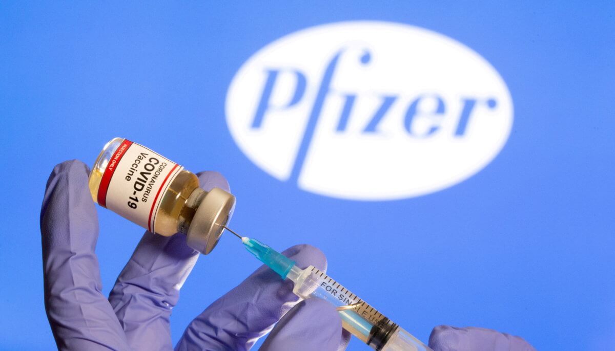 FILE PHOTO: A woman holds a small bottle labeled with a ‘Coronavirus COVID-19 Vaccine’ sticker and a medical syringe in front of displayed Pfizer logo in this illustration