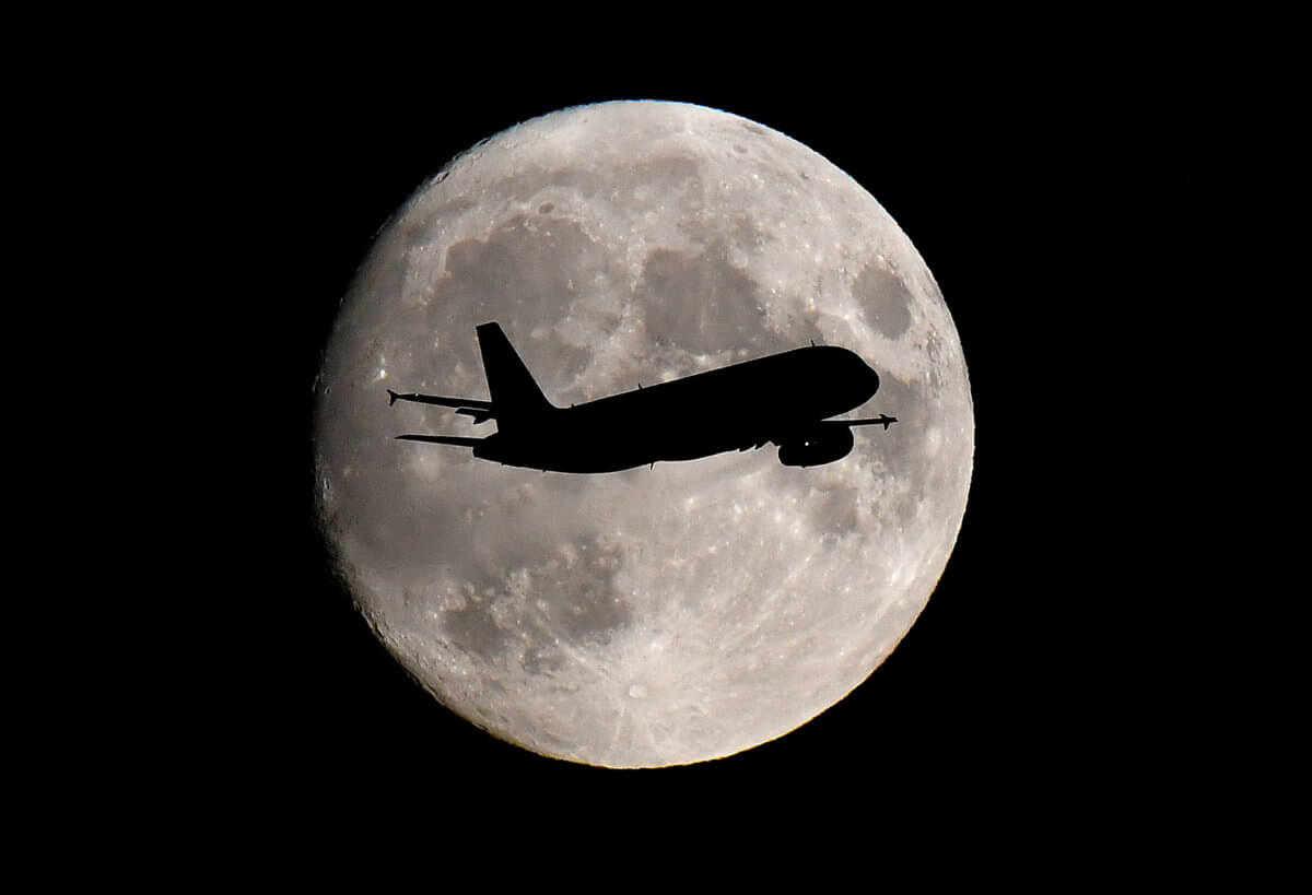FILE PHOTO: A passenger plane passes in front of the moon as it makes its final landing approach to Heathrow Airport in London