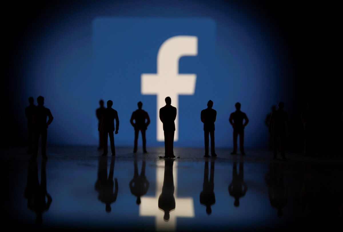 Small toy figures are seen in front of displayed Facebook logo in this illustration