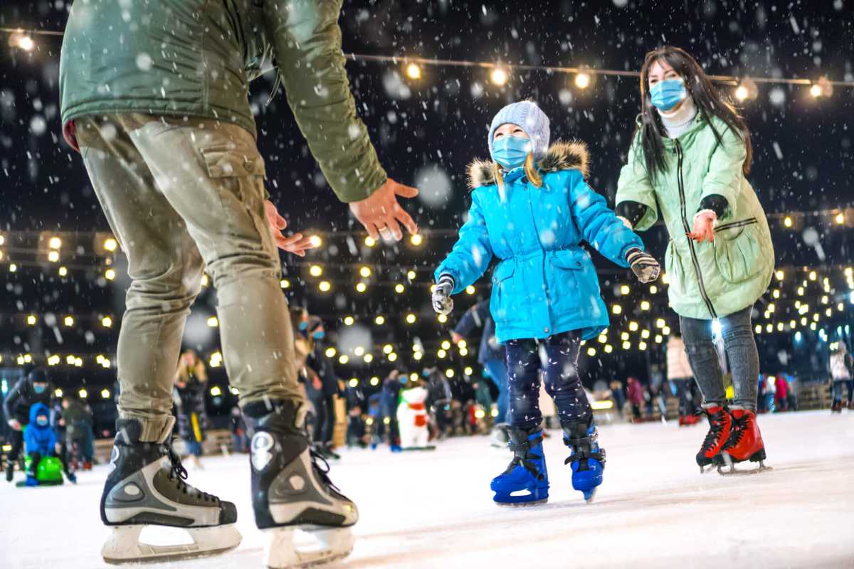 Skating rink. Family wearing the medical face masks on the ice rink. Prevention of coronavirus and other infectious diseases during the winter holidays concept. Mom and dad teach daughter to skate.