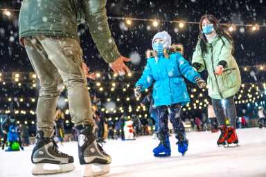 Skating rink. Family wearing the medical face masks on the ice rink. Prevention of coronavirus and other infectious diseases during the winter holidays concept. Mom and dad teach daughter to skate.