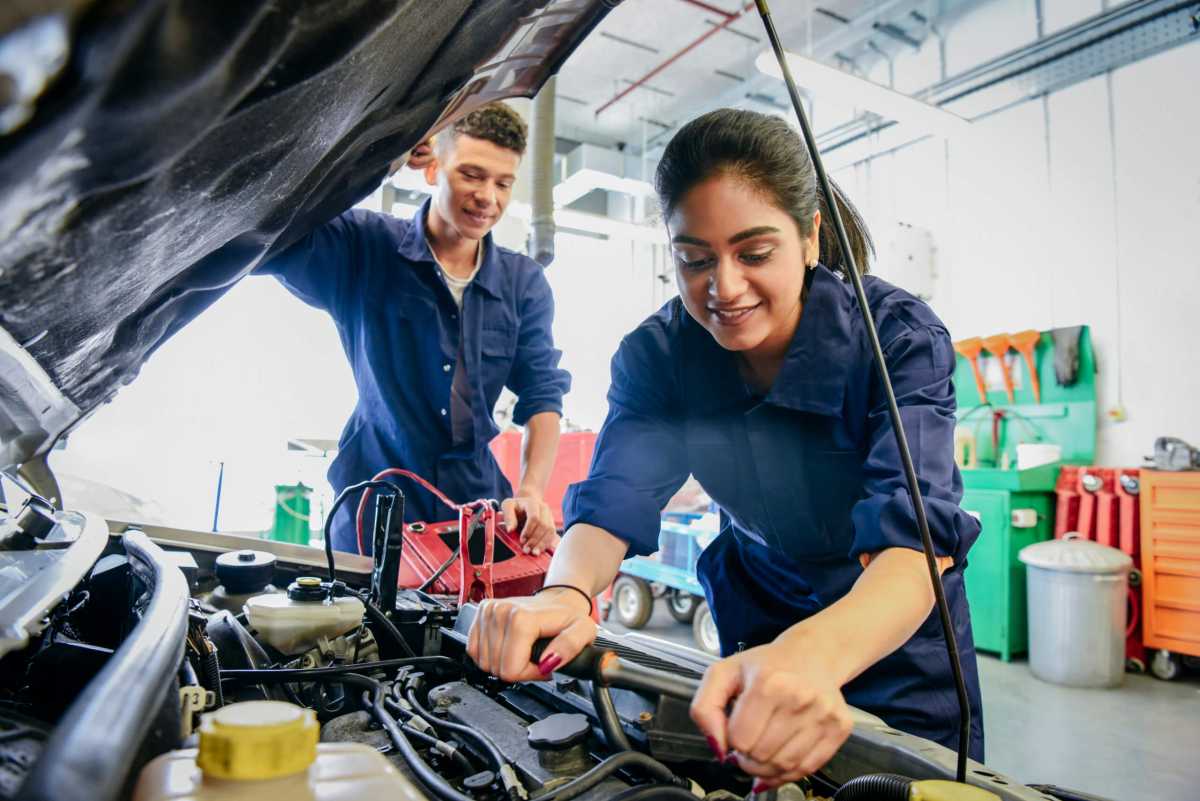 Female mechanic fixing car, young man watching
