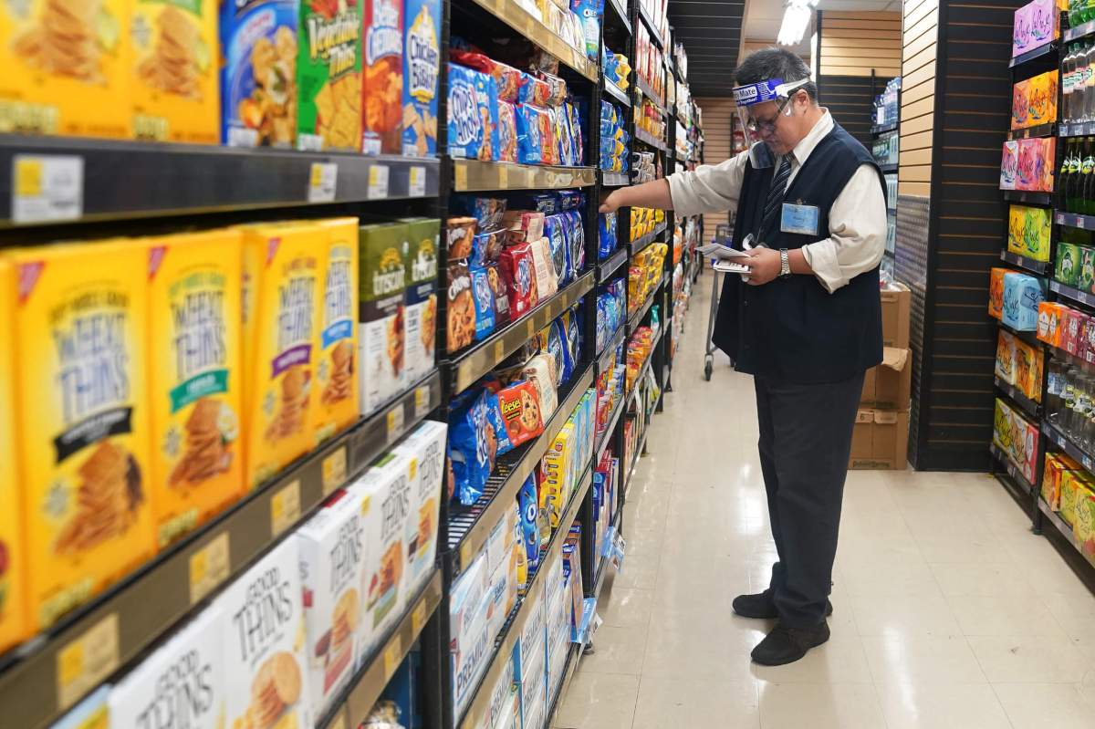 FILE PHOTO  – A worker with a face shield checks products on the shelf of a grocery store