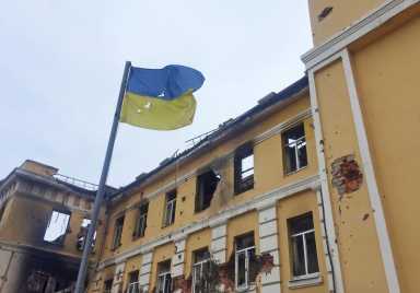 The Ukrainian national flag is seen in front of a school which, according to local residents, was on fire after shelling in Kharkiv