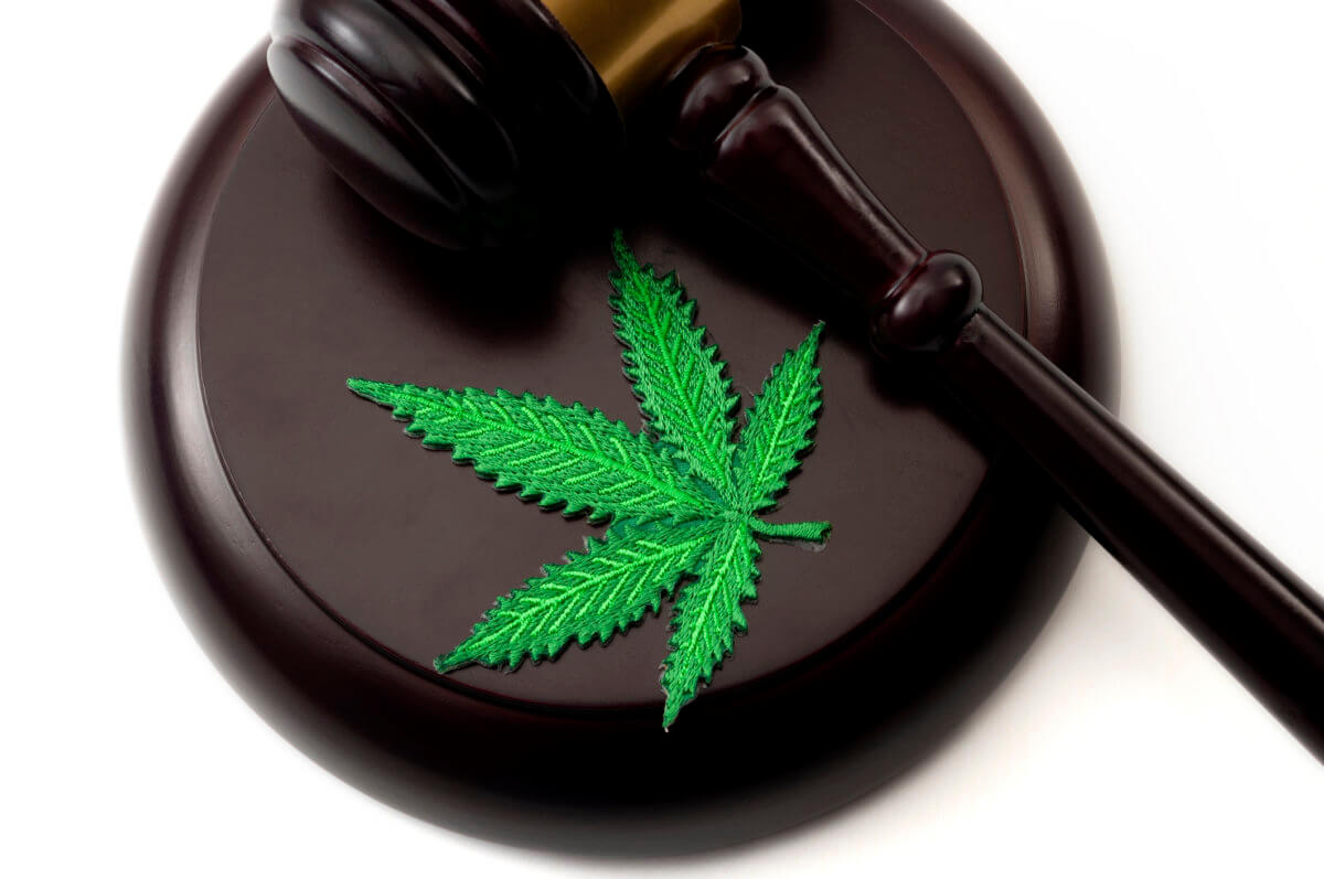 Legal weed, decriminalized pot or felony conviction for possession of a schedule one drug concept theme with a marijuana leaf and a wooden gavel isolated on white background