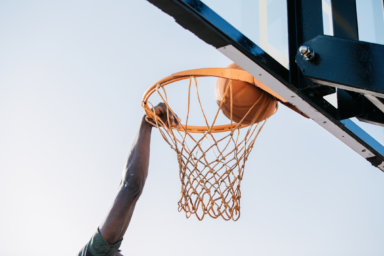 A basketball player’s hand grips the edge of the hoop he scores