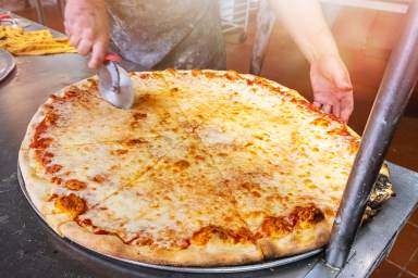 Pizzaiolo in New York cutting a giant cheese pizza to take out