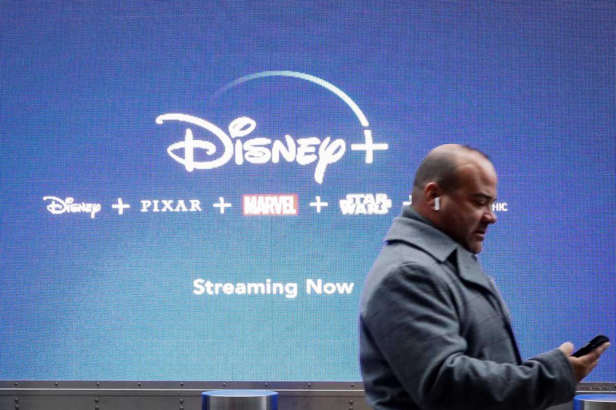 A man looks at his phone as he passes by a screen advertising Walt Disney’s streaming service Disney+ in New York