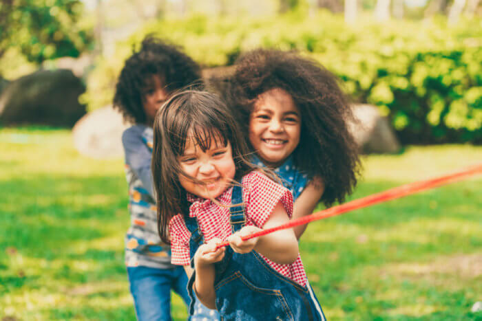 Happy children playing tug of war and having fun during summer camping in the park.