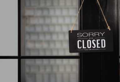 Signboard of tell sorry we are closed business and please come back again when situation improved with hanging to door front at shop.