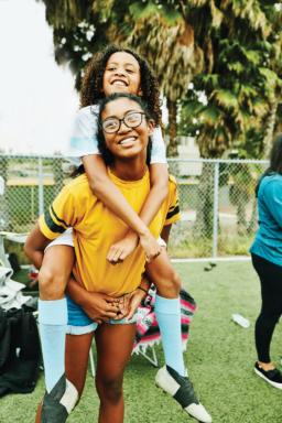 Smiling young female soccer player riding piggy back on older sister after game