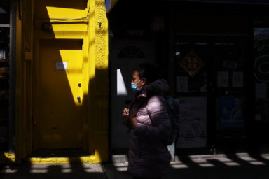 Woman, wearing a protective mask, walks past a building in the Cypress Hills section of the Brooklyn borough of New York City