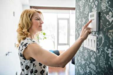 Smiling Woman Adjusting Thermostat On Home Heating System