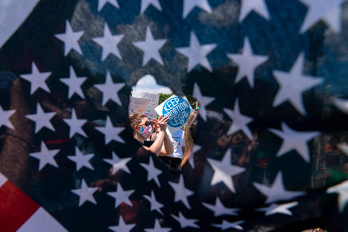 Abortion rights activists are seen through a hole in an American flag as they protest outside the Supreme Court in Washington, Saturday, June 25, 2022. The Supreme Court’s decision to overturn national protections for abortion has set off a contest between Democratic and Republican lawmakers over whose policies would do more to help vulnerable mothers and children. It's a key issue going into the midterm elections.
