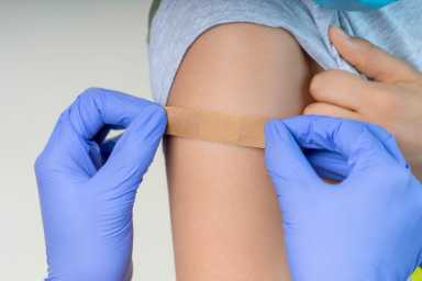 Nurse in rubber protective gloves putting bandage plaster on teenager arm after vaccination. Injection covid vaccine
