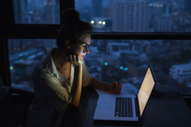 Woman is working with laptop at home during night.