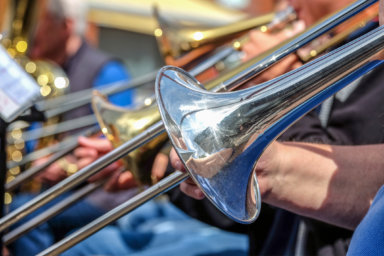 Close-up view: Musicians of a trombone choir or brass band playing their instruments outdoors, selective focus
