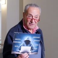 Senator Chuck Schumer holds up a sign with a symbolic hacker on it.