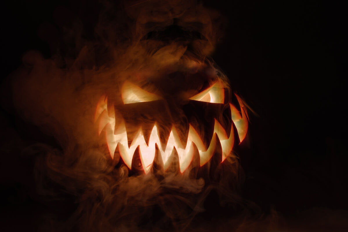 Fuming bright Jack-o’-lantern pumpkin on dark solid background. Glowing eyes and a terrible grin. Halloween minimal concept. Copy space. Desktop wallpapers
