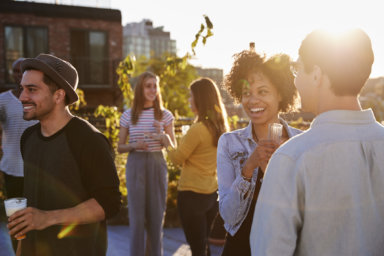 Happy friends at a rooftop party backlit by sunlight