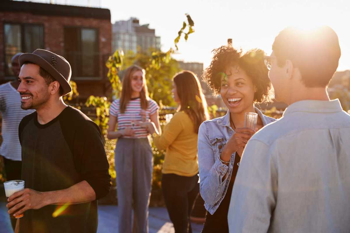 Happy friends at a rooftop party backlit by sunlight