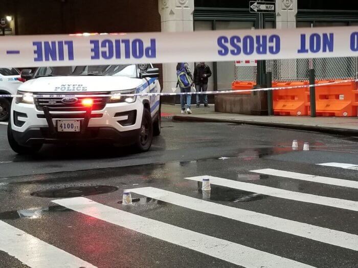 Police tape cordons off a street with an NYPD cruiser