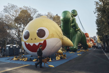 Police walk by inflated helium balloons of Baby Shark and Sinclair's Dino on Wednesday, Nov. 23, 2022, in New York