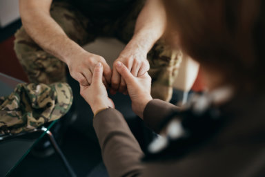 Close-up of psychotherapist holding hands with a soldier during counseling at her office.
