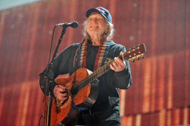 Willie Nelson playing a guitar on stage.