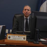 Former Correction Commissioner Louis Molina sitting at desk with nameplate