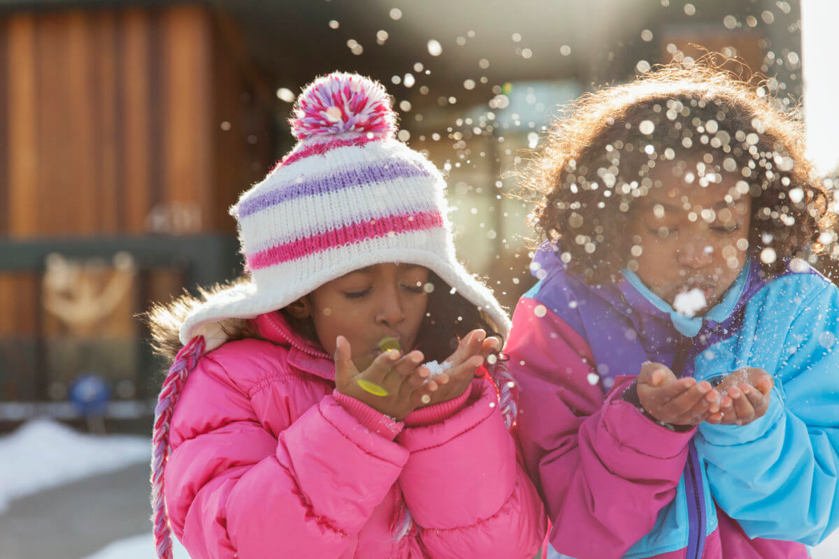Cute little sisters blowing snowflakes outdoors
