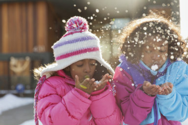 Cute little sisters blowing snowflakes outdoors