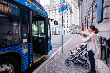 A woman stands outside of an MTA bus with a stroller.