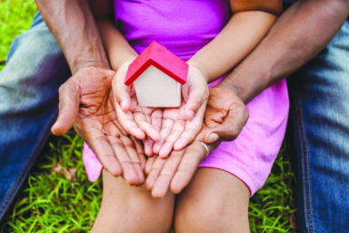 Hands of family together holding house in green park