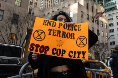 A protester holding an orange sign that reads "End Police Terror, Stop Cop City."