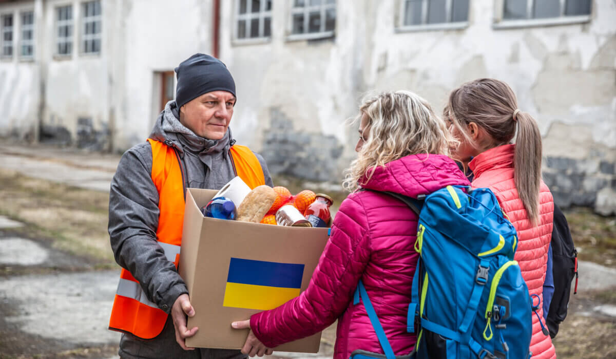 Volunteer in orange west gives a box of food donation to fleeing refugees from Ukraine.