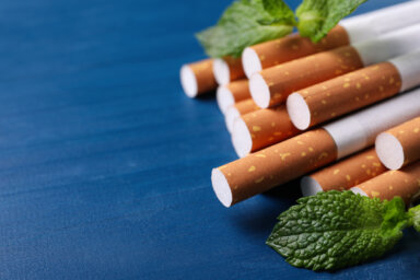 Menthol cigarettes and mint leaves on blue wooden table, closeup. Space for text