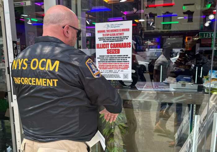 An Office of Cannabis Management enforcement officer posts a sign after a store was raided in Manhattan for illegal pot sales on June 7, 2023.