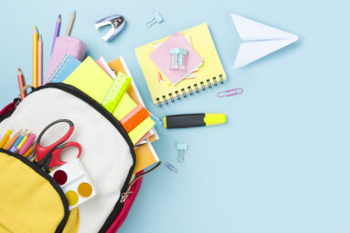 Many colorful school supplies and backpack arranged on blue background