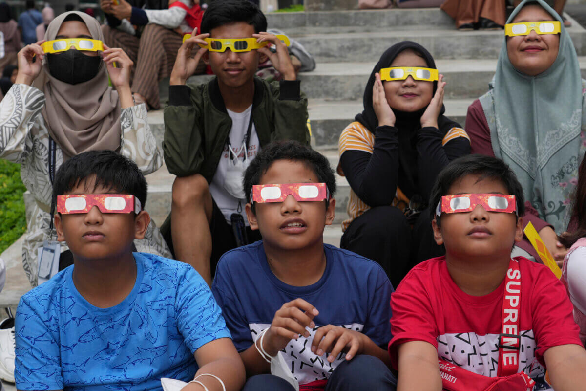 Youths wear protective glasses to watch a hybrid solar eclipse in Jakarta, Indonesia