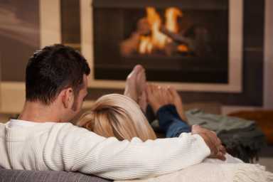 A man and woman sitting in front of a fire, like couples would during cuffing season.