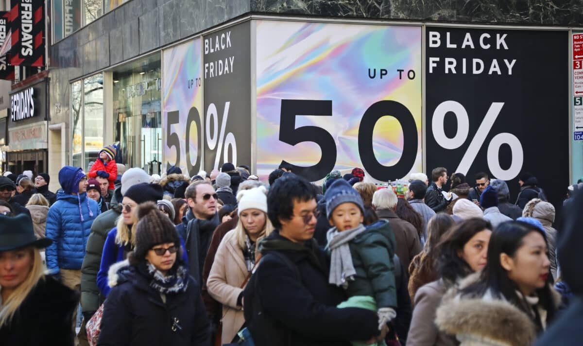 Crowds walk past a large store sign displaying a Black Friday discount in midtown Manhattan,