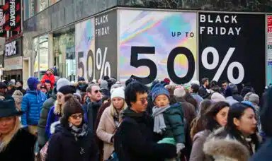 Crowds walk past a large store sign displaying a Black Friday discount in midtown Manhattan,