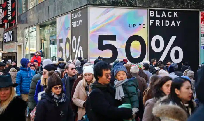 Crowds walk past a large store sign displaying a Black Friday discount in midtown Manhattan,