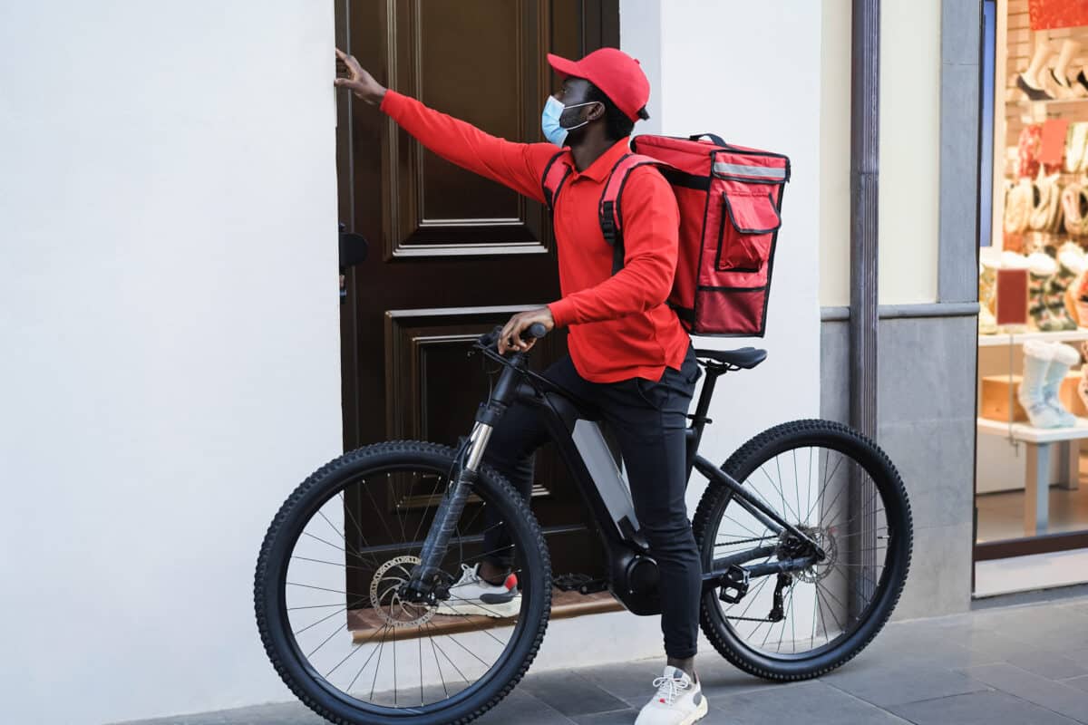 African delivery man with electric bike ringing the doorbell – Focus on face