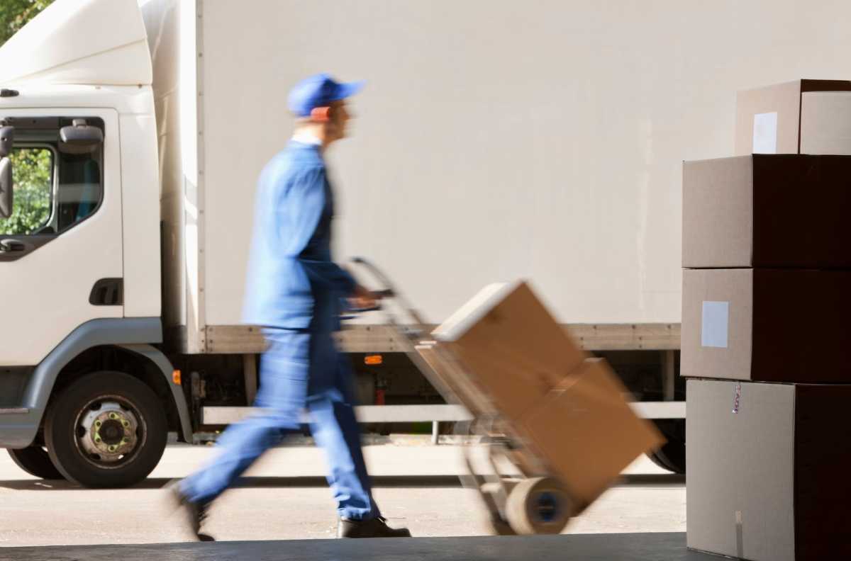 Side view of worker with push cart outside warehouse
