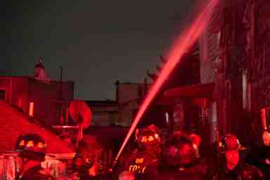 Firefighters direct a hose stream on the outside of a burning building during a fatal car fire.